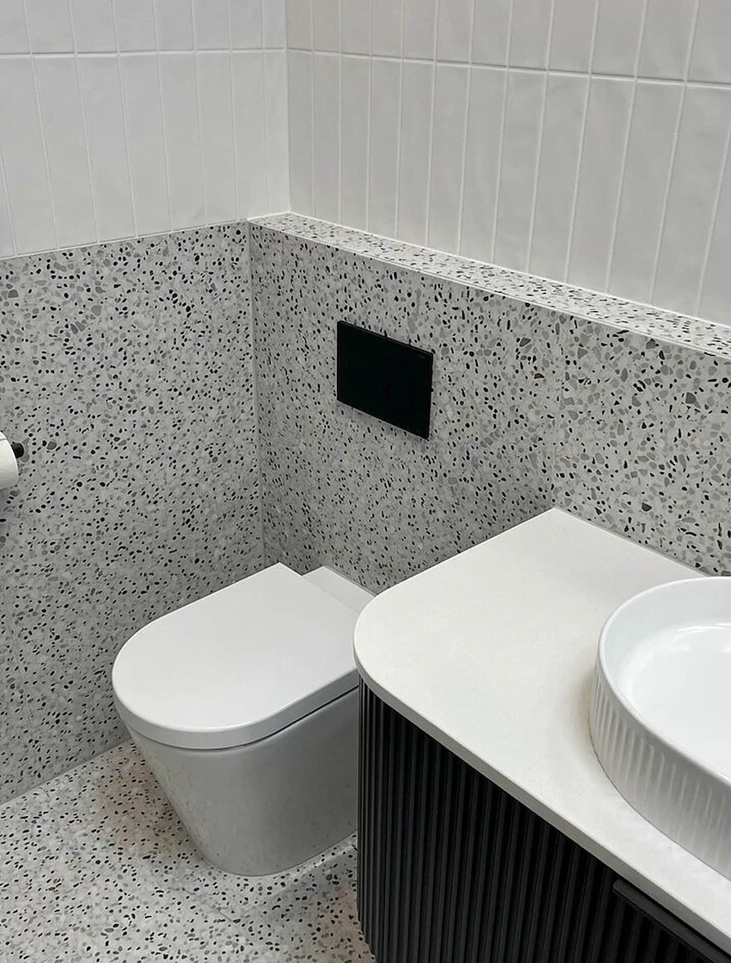 Powder room with terrazzo floor and wall tiles below white vertical stack-bond tiles