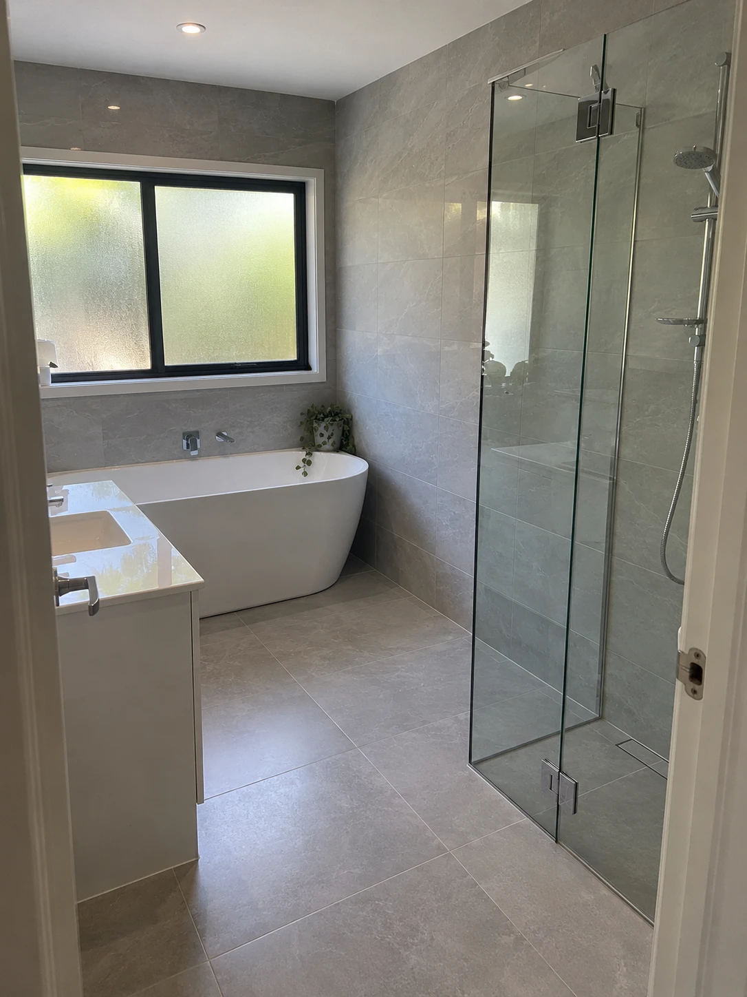 Bathroom with large-format grey stone-look floor and wall tiles, a freestanding bath and a frameless walk-in shower