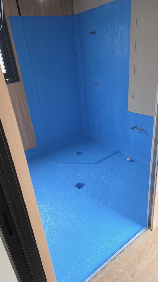 Shower recess coated in blue waterproofing membrane before tiling, with the floor waste and wall outlets visible